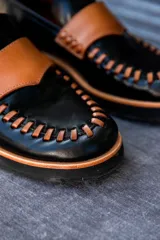 Mocasín de diseño único en colores negro, camel y dorado, con detalles de costura.