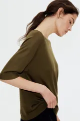 Remera color verde oliva de punto, con corte holgado, cuello redondo y mangas cortas raglán al codo.