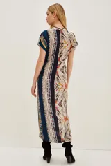 Vestido midi estampado con cuello en V y mangas cortas. Presenta un diseño con cordón ajustable a la cintura y abertura frontal en la falda. El estampado es de estilo étnico o tribal en tonos beige, negro, amarillo y rojo.