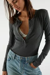 Camiseta tipo henley de manga larga, color blanco, confeccionada en algodón elástico con cuello redondo y tapeta de botones.