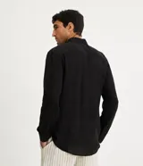 Camisa negra de lino con corte clásico, cuello camisero y mangas largas. Cierre frontal con botones.