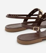 Sandalia marrón de cuero sintético, con tiras finas, apliques de conchas doradas y cierre con hebilla.