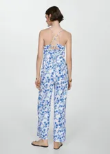 Mono largo blanco con estampado floral azul, escote de pico y tirantes finos cruzados en la espalda.