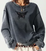 Sweater gris con efecto gastado y aplique de encaje negro con forma de mariposa en el frente.