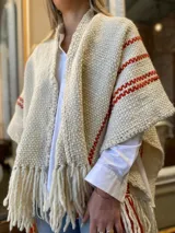 Ruana color crema tejida en lana merino con rayas horizontales color ladrillo y flecos largos en el ruedo.