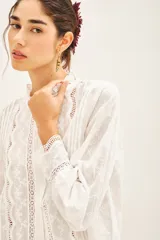 Camisa blanca de broderie con cuello alto y cartera en el frente. Detalles de puntillas y alforzas en el delantero y corte regular.