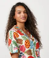 Conjunto de camisa y short de viscosa con estampado tropical de flores, frutas y follaje. La camisa es de manga corta con cuello bowling y botonadura frontal. El short es de corte clásico con cintura elástica.