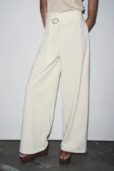 Pantalón de tiro alto color crema, de corte palazzo, con cinturón ancho de tela con hebilla metálica.