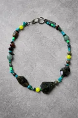 Collar corto de piedras naturales, con cuentas facetadas grandes de color verde oscuro/negro, cuentas redondas de jade verde claro, cuentas amarillas, cuentas turquesas, cuentas marrones y cuentas pequeñas cuadradas de color verde neón. Cierre de mosquetón metálico con dije de marca grabado.
