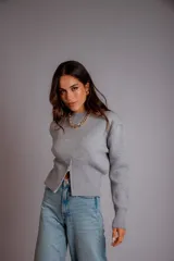 Buzo gris de punto con cuello redondo, mangas largas abullonadas y cierre frontal asimétrico.