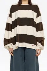 Camiseta de manga larga con corte oversize y escote redondo. Presenta un patrón de rayas horizontales anchas en color marrón oscuro y beige claro. Posee un pequeño logo bordado en la parte inferior derecha.