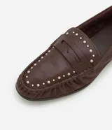 Mocasín de cuero color marrón con puntera fina, detalle de pliegues y tachuelas plateadas.