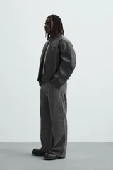 Pantalón de algodón color gris oscuro con efecto lavado, corte relaxed fit y pierna ancha. Presenta bolsillos delanteros, bolsillos traseros de plastrón y un bolsillo lateral con cierre de cremallera en la pierna.