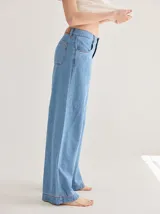 Pantalón gris de tiro medio alto, corte ancho, con bolsillos delanteros y traseros, detalles de atraques y triples costuras en color amarillo.