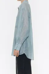 Camisa larga de viscosa con textura, de corte recto, con cuello camisero, manga larga de puño con botón y cierre frontal con abotonadura. Presenta bolsillo de plastrón en el pecho y nudo decorativo en la parte trasera para dar volumen.