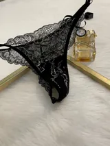 Conjunto de lencería de encaje negro con blanco, compuesto por un corpiño triangular con breteles regulables y cierre de gancho delantero, y una tanga regulable.