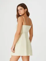 Vestido corto color amarillo pálido, con breteles finos, escote en V cruzado y lazo en la cintura.
