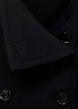 Abrigo negro de paño con doble botonadura, cuello con solapas y dos bolsillos laterales.