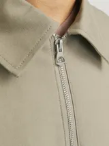 Chaqueta color beige de manga larga con cuello clásico, cierre frontal con cremallera y bolsillos laterales.