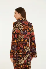 Camisa negra con estampado floral en tonos naranja, rojo y amarillo. Corte recto y fluido con cierre frontal con botones. Cuello clásico y manga larga.