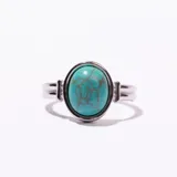Anillo de metal plateado con piedra ovalada de color turquesa veteada, engastada en un bisel simple.
