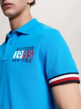 Chomba azul de algodón orgánico elástico, corte slim, con cuello clásico, cartera de dos botones, logo bordado en el pecho y ribetes distintivos en las mangas.