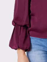 Blusa de gasa satén color bordó, marca Tahari, con cuello alto fruncido y mangas largas abullonadas. La espalda tiene una abertura central con botón.