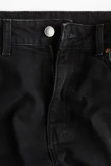 Jean tobillero de denim negro lavado, tiro alto, con cinco bolsillos y cierre de botón. Corte ajustado en cadera y muslo, con pierna recta y levemente ceñida en el bajo.