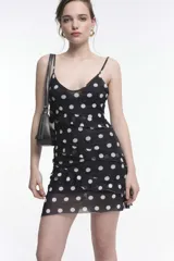 Vestido corto negro con lunares blancos, breteles finos y volados horizontales.