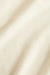 Remera de punto color crema, de corte holgado con hombros caídos y mangas cortas al codo. Presenta cuello redondo y remates acanalados en cuello, puños y bajo.