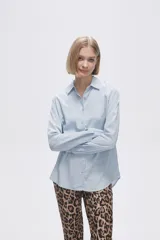 Camisa blanca de manga larga con cuello clásico y cierre frontal con botones. Corte recto y holgado.