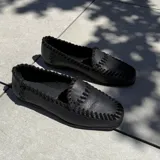 Mocasines negros de cuero vacuno con tientos de cuero pasados a mano y suela de goma.