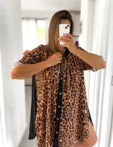 Camisola corta con estampado de leopardo, cuello camisero, cierre frontal con botones y mangas cortas con puños. Presenta paneles laterales negros.