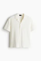 Camisa de manga corta color crema, de punto texturizado de mezcla de algodón de peso medio. Modelo con cuello abierto, tapeta lisa y bajo recto.