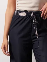 Pantalón negro con estampado de hojas color rosa en el ruedo y cintura elastizada con lazo ajustable.