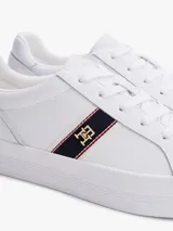 Zapatillas de corte bajo confeccionadas en piel napa color blanco. Presentan una franja lateral de tejido trenzado con los colores distintivos de la marca y una insignia metálica con el monograma TH. Cuentan con cordones al tono, suela de goma vulcanizada y logo en relieve en el talón.