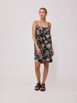 Vestido corto negro con estampado de palmeras, soles y estrellas en color crema. Diseño suelto con breteles finos y escote recto con lazo ajustable.