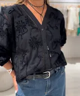 Camisa negra de manga larga con puños elásticos, cierre frontal con botones y apliques bordados de flores en la parte delantera y trasera.