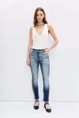Jean de tiro medio-alto, calce slim loose, denim azul con desgaste localizado y bigotes. Galón de brillos en los laterales y ruedo desflecado.