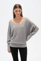 Sweater gris de tejido acanalado, con escote en V amplio y mangas largas estilo murciélago. Presenta pequeños apliques brillantes distribuidos sobre toda la prenda.