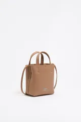 Bolso mini tipo tote de cuero color marrón claro, con estructura blanda y formato vertical. Tiene doble asa corta, correa larga regulable, cierre con cinta, logo metálico de la marca, bolsillo interior con cierre y forro con logo grabado.
