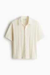 Camisa color crudo de punto pointelle con estilo crochet, de manga corta, cuello inglés, botones frontales y bajo recto.
