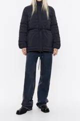 Campera puffer negra con cuello alto, cierre frontal con botones a presión y cordón ajustable en la cintura. Diseño acolchado con corazones.