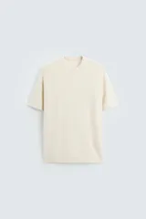 Camiseta color crema de punto con hilatura de algodón, corte regular fit, cuello redondo, manga corta y terminaciones en rib.