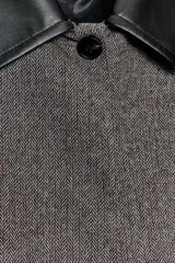 Chaqueta corta de tweed gris con cuello solapa y puños de cuero negro. Cierre frontal con botones ocultos.