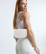 Bolso pequeño estructurado, modelo shoulder, color blanco con textura capitoneada. Tiene correa de cadena dorada, bolsillo interior con cierre y tapa con botón a presión.