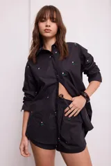 Camisa negra con bordado de flores rosas, corte recto, cuello clásico y cierre frontal con botones.