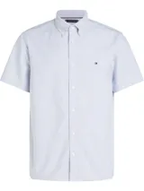 Camisa de manga corta Tommy Hilfiger Heritage, de corte regular, confeccionada en tela Oxford a rayas verticales celestes y blancas. Tiene cuello abotonado, cierre con botones y logo de Tommy Hilfiger bordado en el pecho.