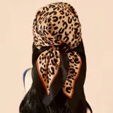 Pañuelo cuadrado de tela satinada con estampado animal print en tonos beige y negro, con borde negro y detalles en naranja.
