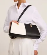 Cartera shoulder mediana de cuero sintético, con diseño bicolor blanco y negro y detalles metálicos dorados.